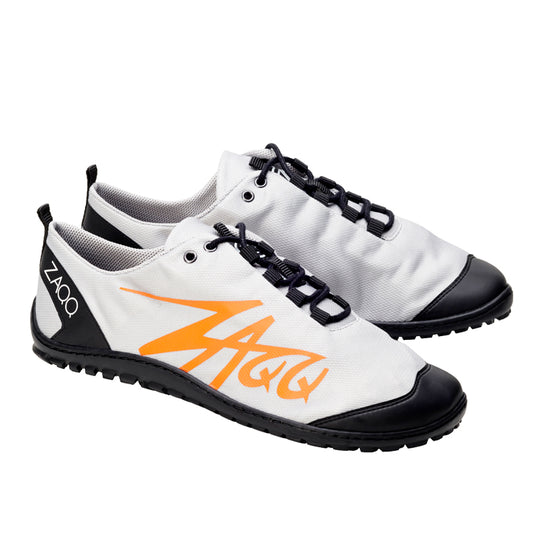 Ein Paar SQIM Grey Orange Sneakers von ZAQQ, mit einer stilvollen Kombination aus Schwarz und Weiß mit orangefarbenen Zickzack-Mustern an den Seiten. Diese veganfreundlichen Sportschuhe sind mit schwarzen Schnürsenkeln, einer schwarzen Zehenkappe und einer strukturierten schwarzen Sohle aus recyceltem Kunststoff gestaltet. Der Markenname ZAQQ ist deutlich auf der Ferse zu sehen.