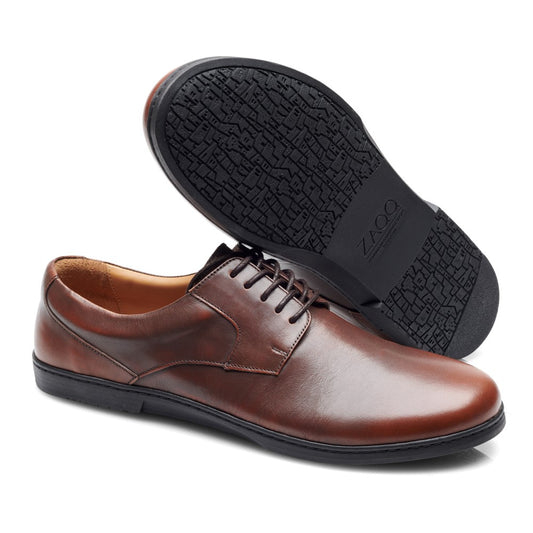 Ein Paar BRIQ Antique Brown Abendschuhe von ZAQQ, gefertigt aus feinem Kalbleder-Leder, wird präsentiert, wobei ein Schuh auf der Seite liegt und eine strukturierte schwarze Sohle freigibt. Diese Schuhe verfügen über ein klassisches Schnürdesign und ein glattes, poliertes Finish, perfekt, um einen eleganten Eindruck zu hinterlassen.