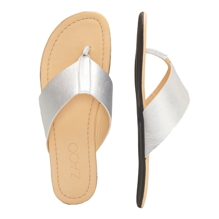 Abgebildet ist ein Paar ZAQQ QOSS Silver Flip-Flop-Sandalen mit hellbraunen Sohlen, wobei eine Sandale von oben und die andere von der Seite betrachtet wird, was das metallische Riemendesign und den zeitlosen Stil hervorhebt. Diese schicken Sandalen bieten mit ihrer flexiblen Sohle zusätzlichen Komfort.