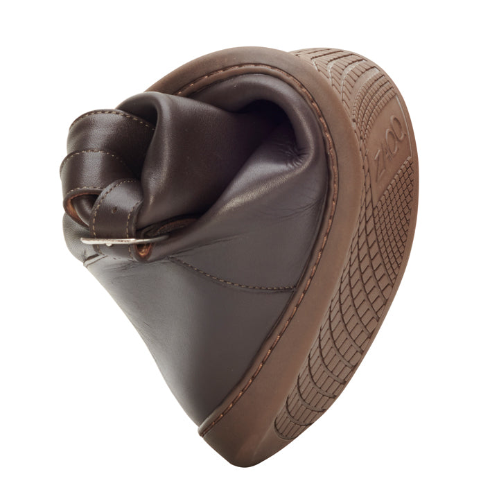 Der ATTRAQT Winter Brown Schuh von ZAQQ ist in der Mitte gebogen und zeigt so seine flexible Sohle und sein Barfußgefühl. Das Profilmuster auf der Sohle verbessert sowohl die Flexibilität als auch den Halt und macht ihn ideal für einen Winterstiefel. Darüber hinaus sind die Nähte und Schnallendetails des Schuhs hervorgehoben, um den Tragekomfort zu verbessern.