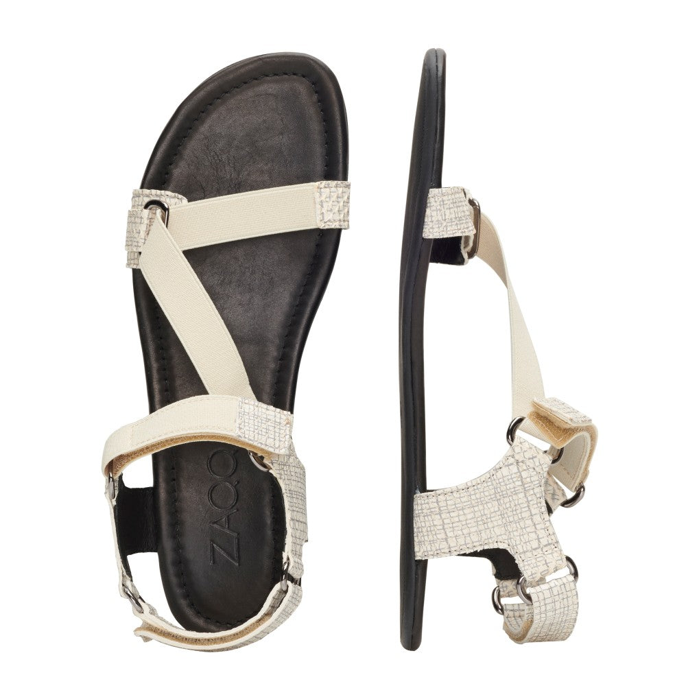 Die MIQA Beige Sandalen von ZAQQ werden aus verschiedenen Blickwinkeln vor einem weißen Hintergrund präsentiert. Diese Barfußsandale verfügen über eine flache schwarze Sohle mit strukturierten Details und verstellbare Riemen, die sich elegant über den Fuß und um den Knöchel kreuzen. Alle sind aus Premium Velours Leder in Beige gefertigt.