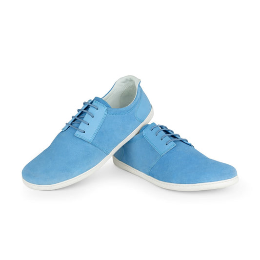 Ein Paar PIQUANT Azure Sneaker von ZAQQ mit samtig-blauem Finish, weißer Sohle und passenden blauen Schnürsenkeln. Ein Schuh lehnt kunstvoll an dem anderen vor einem schlichten weißen Hintergrund.