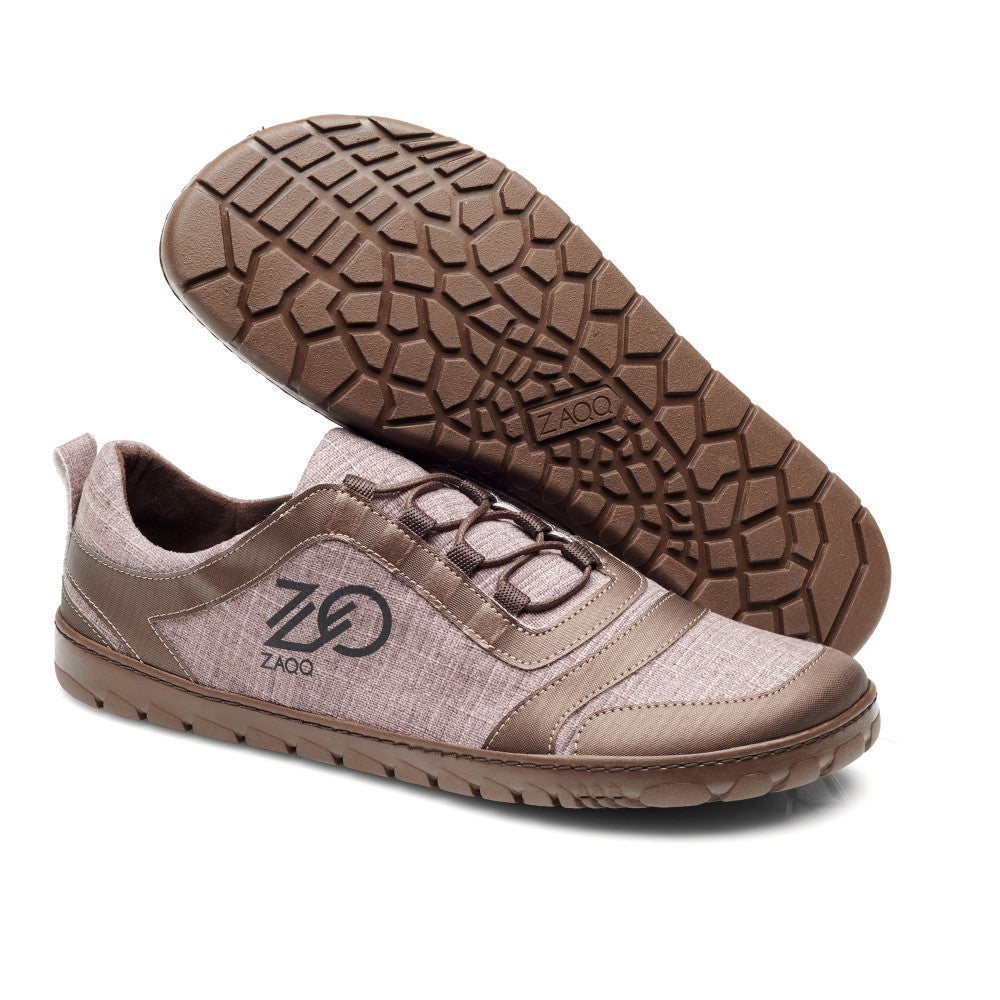 Die SQILL Brown Sneaker von ZAQQ sind Freizeitschuhe aus veganem Obermaterial mit strukturierter Gummisohle. Sie bestechen durch eine Kombination aus Stoff und lederähnlichen Materialien mit dem ZAQQ-Logo auf der Seite. Ein Schuh steht aufrecht und hebt sein Design hervor, während der andere sein detailliertes Sohlenmuster zur Schau stellt.