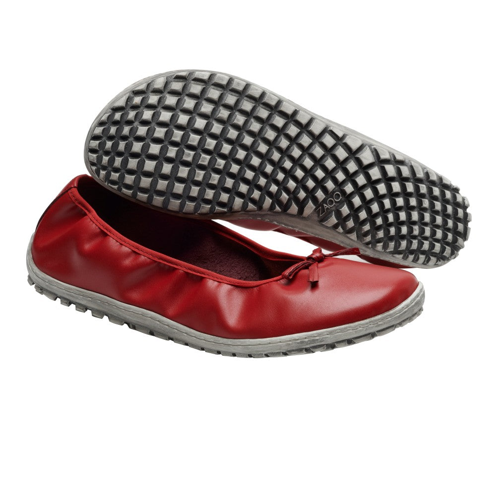 Ein Paar SUQAR Berry Ballerinas von ZAQQ in einem auffälligen Rot mit einer kleinen Schleife oben. Ein Schuh steht aufrecht, während der andere seine strukturierte graue Sohle mit Gittermuster zur Schau stellt. Diese Barfuß-Ballerinas aus glattem Glattleder bieten ein schlichtes und elegantes Design.