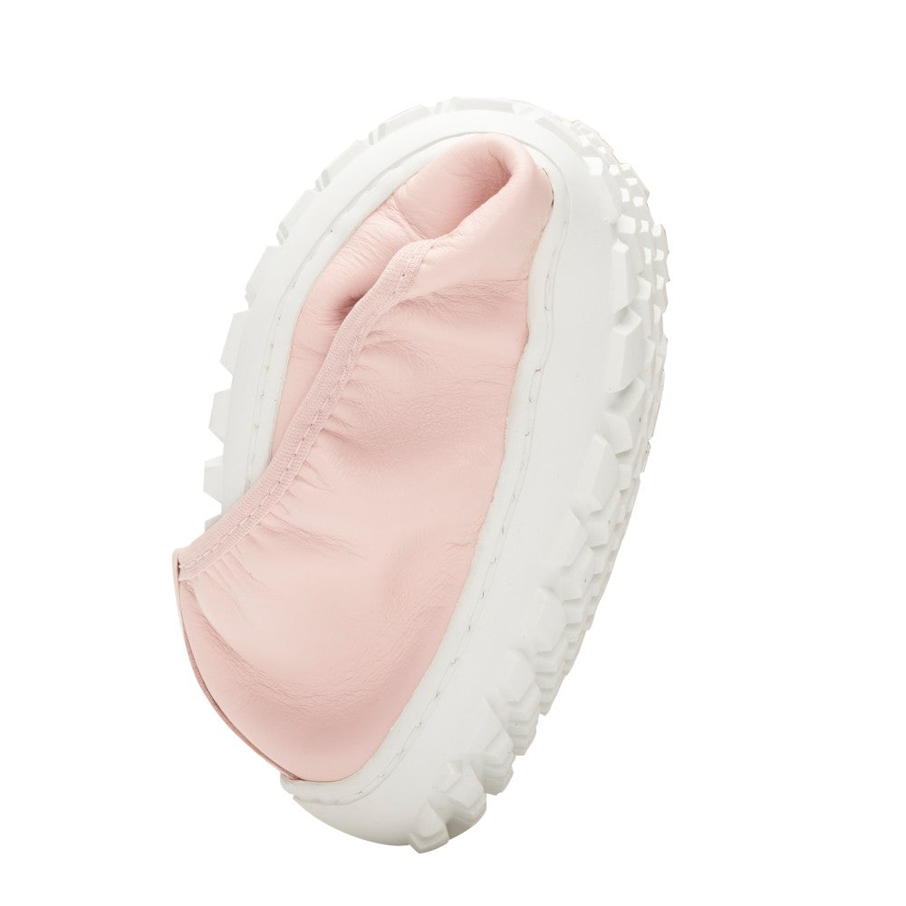 Wir präsentieren den SUQAR Candy von ZAQQ: einen zartrosa Slipper aus Nappaleder mit einer dicken, strukturierten weißen Sohle. Dieser Schuh erinnert an eine Barfuß-Ballerina und ist auf die Seite gefaltet, um seine flexible Sohle und sein einzigartiges Design zu präsentieren.