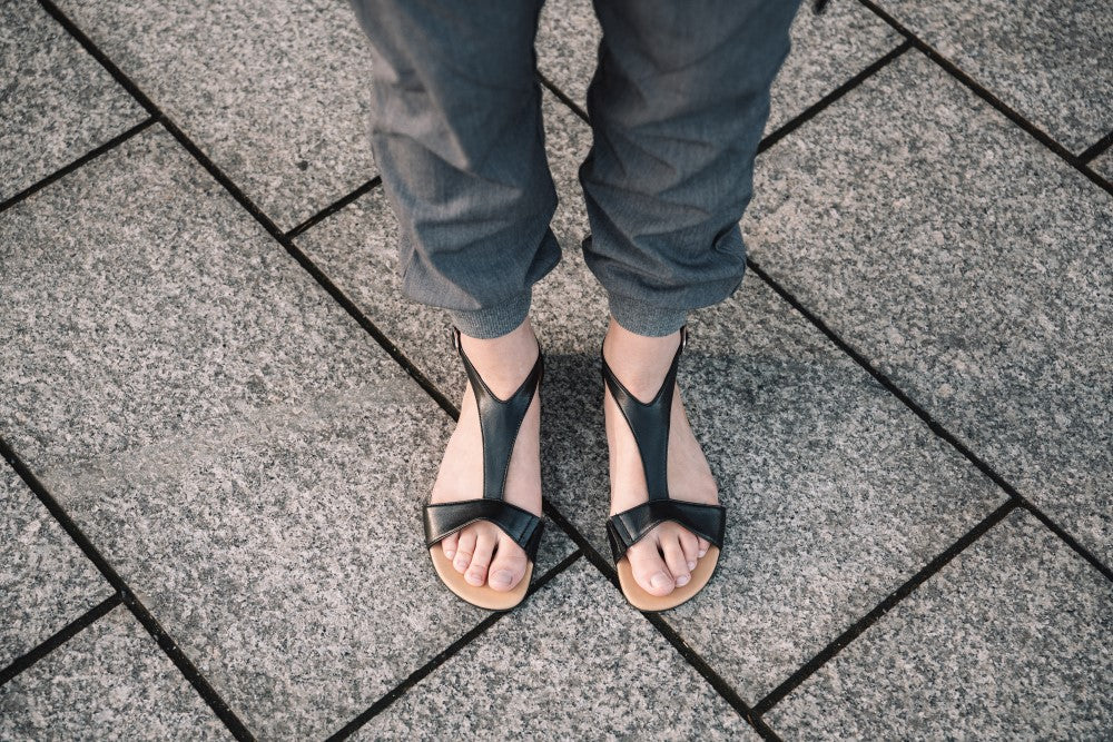 Ein Paar schwarze CLIQ-Sandalen von ZAQQ mit schwarzen Riemen und hellbraunen Sohlen vor weißem Hintergrund.