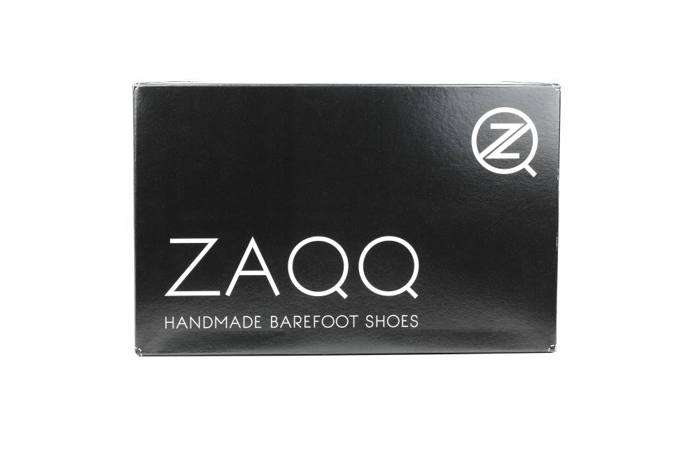 Die Produktverpackung für den QEA Velours Black von ZAQQ besteht aus einem eleganten schwarzen Schuhkarton, auf dem der Markenname ZAQQ in großen weißen Buchstaben deutlich zu sehen ist. Darunter erscheint in kleinerer Schriftgröße der Satz „HANDMADE BAREFOOT SHOES“, der jeden Barfußschuh-Liebhaber anspricht. Darüber hinaus ist in der oberen rechten Ecke das markante ZAQQ-Logo zu sehen: ein stilisiertes Z in einem Kreis.