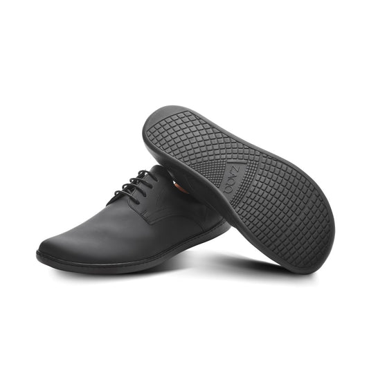 Ein Paar elegante schwarze ZAQQ PEAQ Vegan-Abendschuhe, von denen einer aufrecht steht und der andere geneigt ist, um die strukturierte Sohle zu zeigen. Diese eleganten schwarzen veganen Schuhe haben ein glattes Lederfinish, das durch schwarze Schnürsenkel akzentuiert wird, und sind mit einem atmungsaktiven Microfaserfutter für Komfort und Stil ausgestattet.