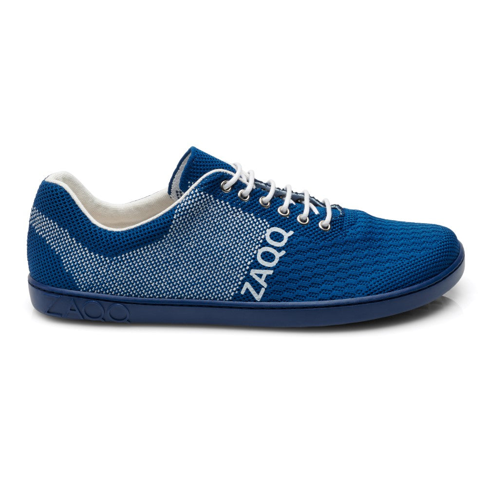 Der QNIT Mare von ZAQQ ist ein blau-weißer Freizeitsneaker aus atmungsaktivem Baumwollstrickgewebe. Er verfügt über eine gewebte Textur und zeigt stolz die Marke ZAQQ auf der Seite. Dieser vegane Barfußschuh hat ein niedriges Profil, weiße Schnürsenkel und eine dunkelblaue Sohle mit dem charakteristischen ZAQQ-Design.