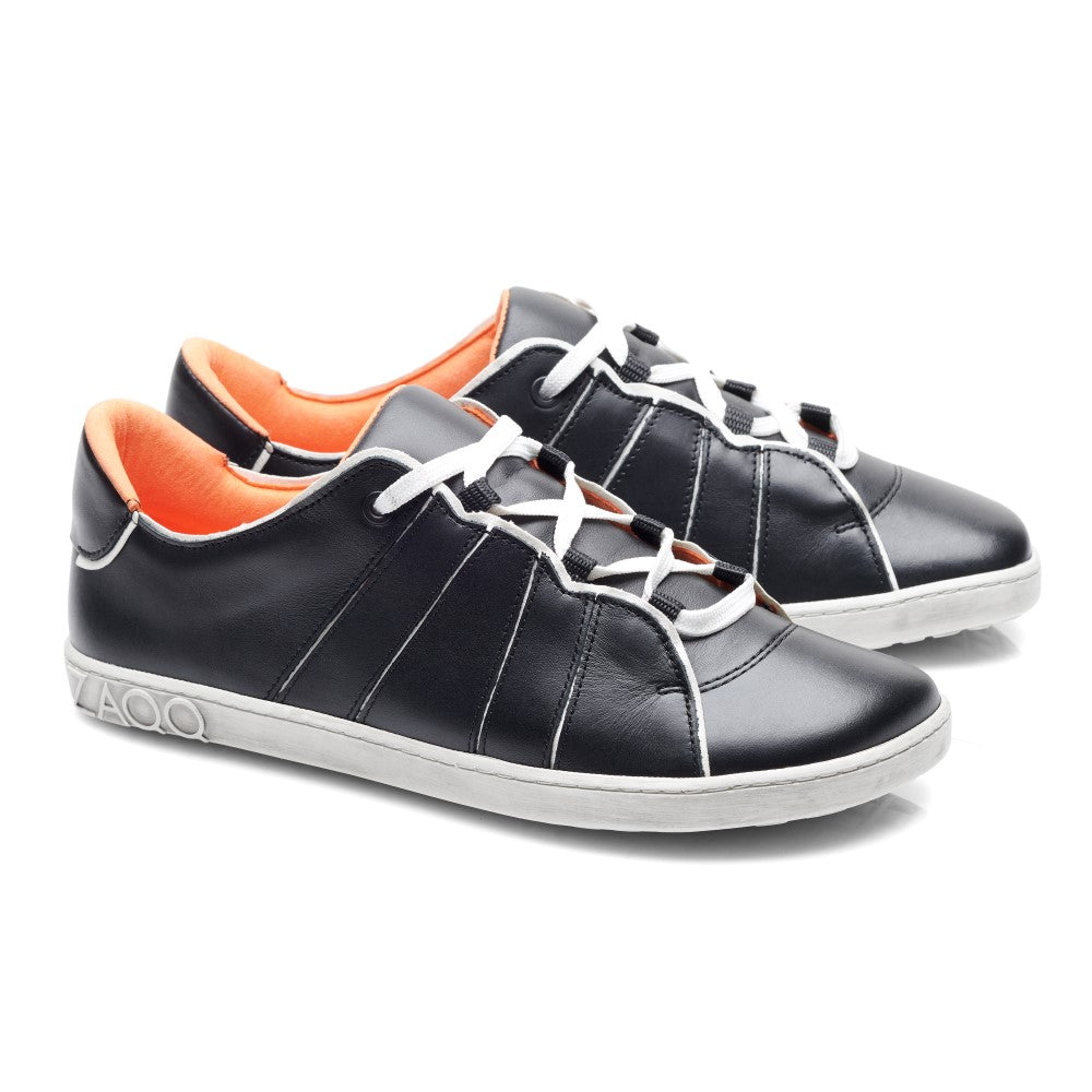 Ein Paar QQQ Low Black White-Sneaker von ZAQQ mit außergewöhnlichem Tragekomfort, gefertigt aus schwarzem Leder mit auffälligen weißen Schnürsenkeln und Sohlen. Die Innenseite ist in einem leuchtenden Orange gehalten und wird durch dekorative weiße Nähte an den Seiten hervorgehoben. Die Schuhe sind so positioniert, dass sie sowohl von der Seite als auch von vorne gut aussehen.